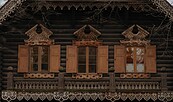 Fassade eines dunklen Holzhauses mit geschnitzten Verzierungen, geöffneten Fensterläden und Balkonbrüstung., Foto: Julia Nimke, Lizenz: PMSG
