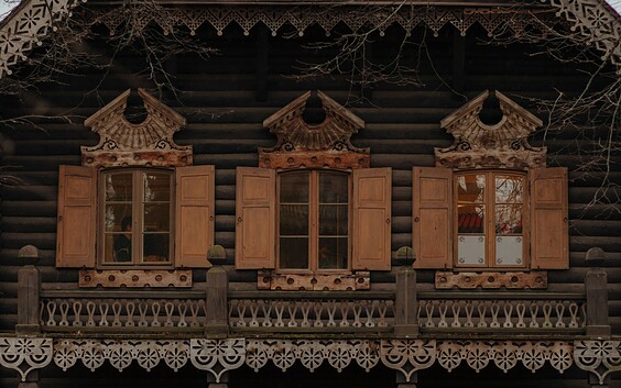 Fassade eines dunklen Holzhauses mit geschnitzten Verzierungen, geöffneten Fensterläden und Balkonbrüstung., Foto: Julia Nimke, Lizenz: PMSG