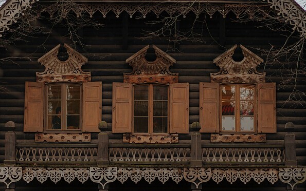 Fassade eines dunklen Holzhauses mit geschnitzten Verzierungen, geöffneten Fensterläden und Balkonbrüstung., Foto: Julia Nimke, Lizenz: PMSG