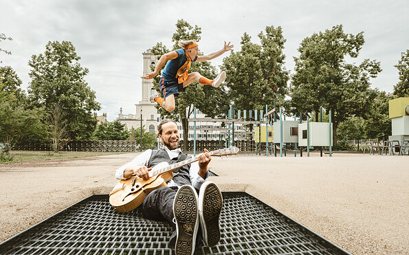 Mann mit Gitarre auf einem Trampolin, dahinter springt ein Mensch, Foto: der bunte hund, Lizenz: der bunte hund