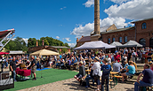 Menschen sitzen und stehen bei einem Fest mit Zelten und einer alten Fabrik im Hintergrund unter blauem Himmel mit Wolken., Foto: Erste Bernauer Braugenossenschaft e. G., Lizenz: Erste Bernauer Braugenossenschaft e. G.