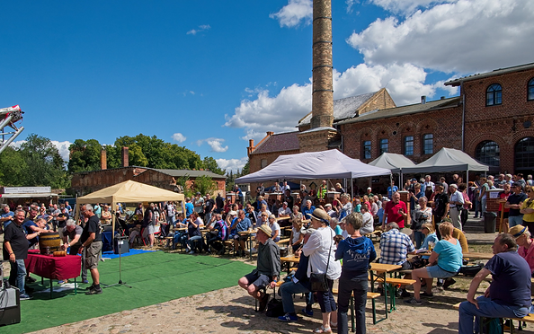 Menschen sitzen und stehen bei einem Fest mit Zelten und einer alten Fabrik im Hintergrund unter blauem Himmel mit Wolken., Foto: Erste Bernauer Braugenossenschaft e. G., Lizenz: Erste Bernauer Braugenossenschaft e. G.