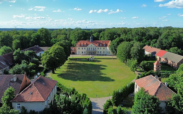 Luftaufnahme vom Schloss Grochwitz mit rotem Dach, großer Wiese, Nebengebäuden und dichtem Wald unter blauem Himmel., Foto: Bettina Unterkofler, Lizenz: Bettina Unterkofler