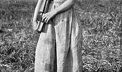 Ein Schulmädchen in wendischer Tracht steht mit Schulbüchern in der Hand barfuß auf einer Wiese. Altes schwarz-weiß Foto, Foto: Denis Galloway, Lizenz: Ethnographical Museum of Transylvania, Romania