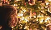 Kind guckt auf den geschmückten Weihnachtsbaum mit Lichterkette, Foto: unsplash.com/de/@greg_rosenke, Lizenz: Netzeband Kultur