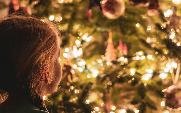 Kind guckt auf den geschmückten Weihnachtsbaum mit Lichterkette, Foto: unsplash.com/de/@greg_rosenke, Lizenz: Netzeband Kultur