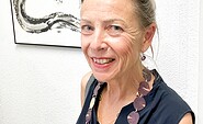 Die Künstlerin steht vor einer weißen Wand und einem ihrer Werke, das japanische Tuschkunst Sumi-e zeigt, Foto: Monika Ruppel, Lizenz: Landhaus Alte Schmiede