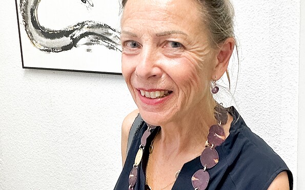 Die Künstlerin steht vor einer weißen Wand und einem ihrer Werke, das japanische Tuschkunst Sumi-e zeigt, Foto: Monika Ruppel, Lizenz: Landhaus Alte Schmiede