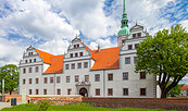 Weißes Schloss mit roten Ziegeldächern, Stufengiebeln und grünem Turm vor wolkigem Himmel; Baum im Vordergrund., Foto: Andreas Franke, Lizenz: Andreas Franke