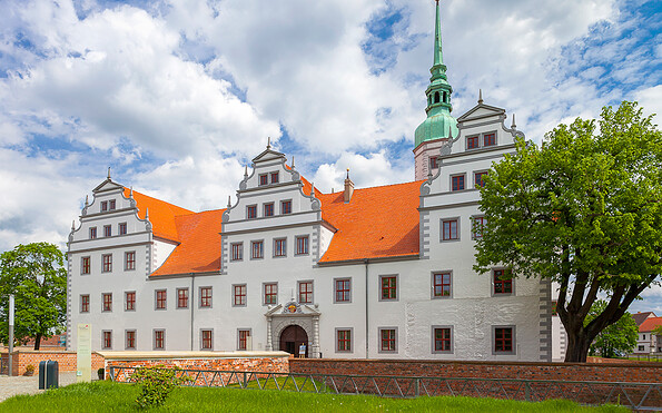 Weißes Schloss mit roten Ziegeldächern, Stufengiebeln und grünem Turm vor wolkigem Himmel; Baum im Vordergrund., Foto: Andreas Franke, Lizenz: Andreas Franke