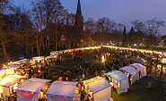 Beleuchteter Weihnachtsmarkt am Abend vor einer Kirche, mit vielen Besuchern, weißen Zelten und kahlen Bäumen., Foto: André Stiebitz, Lizenz: PMSG