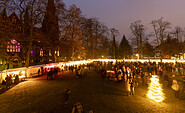 Abendlicher Weihnachtsmarkt mit beleuchteten Ständen und vielen Menschen vor einer Kirche zwischen kahlen Bäumen., Foto: André Stiebitz, Lizenz: PMSG