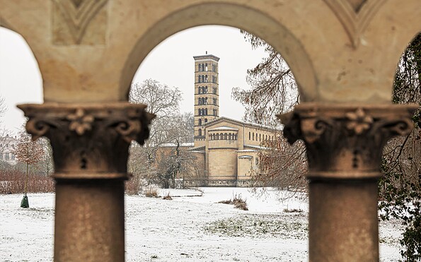 Verschneiter Park mit Kirchturm im Hintergrund, gesehen durch leicht unscharfe steinerne Bögen und Säulen im Vordergrund., Foto: André Stiebitz, Lizenz: PMSG