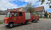 Rotes Feuerwehrfahrzeug mit Anhänger auf Kopfsteinpflaster vor Fachwerkhäusern unter bewölktem Himmel., Foto: Sandra Fonarob, Lizenz: Tourismusverband Dahme-Seenland e.V.