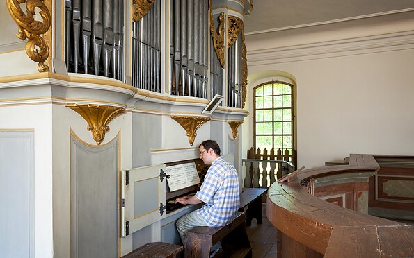 Mann spielt auf der Kirchenorgel mit großen Orgelpfeifen und goldenen Verzierungen; rechts ein hohes Fenster., Foto: Andreas Franke, Lizenz: Andreas Franke
