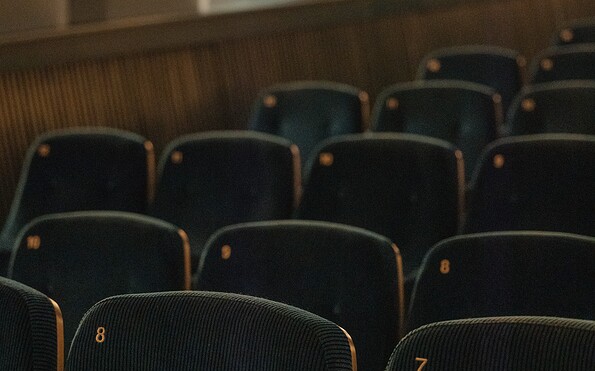 Reihen dunkler gepolsterter Kinosessel mit orangefarbenen Sitznummern, unscharf im Hintergrund., Foto: Julia Nimke, Lizenz: PMSG