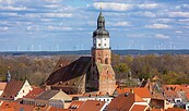 Kirchturm über roten Dächern einer Stadt, dahinter Wald und Windräder unter blauem, wolkigem Himmel., Foto: Andreas Franke, Lizenz: Andreas Franke