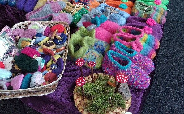 Bunte gefilzte Hausschuhe und Wollaccessoires liegen in Körben und Regalen, daneben rote Fliegenpilz-Deko., Foto: Marlene Prenzel, Lizenz: Marlene Prenzel