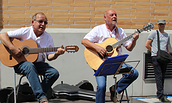 Zwei Männer sitzen vor einer hellen Wand und spielen akustische Gitarren, ein weiterer Mann steht im Hintergrund mit einer Tasche über der Schulter, Foto: Kerstin Grubert, Lizenz: Kerstin Grubert