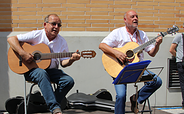 Zwei Männer sitzen vor einer hellen Wand und spielen akustische Gitarren, ein weiterer Mann steht im Hintergrund mit einer Tasche über der Schulter, Foto: Kerstin Grubert, Lizenz: Kerstin Grubert