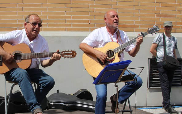 Zwei Männer sitzen vor einer hellen Wand und spielen akustische Gitarren, ein weiterer Mann steht im Hintergrund mit einer Tasche über der Schulter, Foto: Kerstin Grubert, Lizenz: Kerstin Grubert