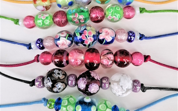 Mehrere bunte Perlenarmbänder mit Glasperlen und Blumenmustern auf farbigen Bändern, auf hellem Hintergrund., Foto: Georg Goes, Lizenz: Museumsverein Glashütte