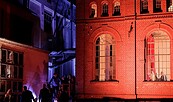 Nachtszene mit rot beleuchtetem Backsteingebäude, blau angestrahlter Fassade und Menschen auf einer Treppe im Hof., Foto: Roxane Adler, Lizenz: Roxane Adler