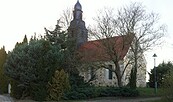 Kirche mit Zwiebelturm und rotem Dach, teils von Bäumen und Sträuchern verdeckt., Foto: TVEEL, Lizenz: TVEEL