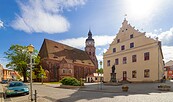 Kopfsteinpflasterplatz mit Backsteinkirche, Kirchturm, hellem Giebelhaus und Statue unter blauem Himmel., Foto: Andreas Franke, Lizenz: Andreas Franke